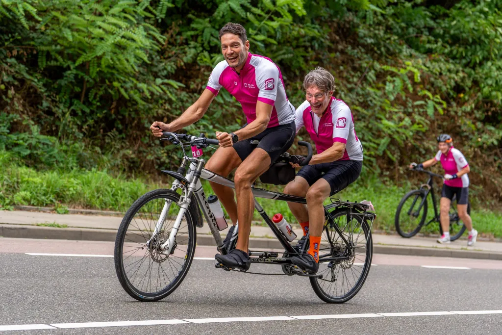Twee mannen fietsen op een tandem een berg op tijdens Bike en Hike voor Parkinson 2026.